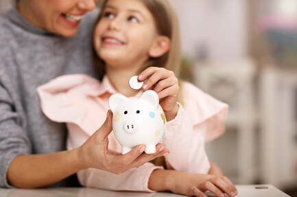 Picture of a mother holding her daughter while the child places a coin inside her piggy bank