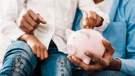 Picture of child sitting on father's lap while putting a coin into a piggy bank
