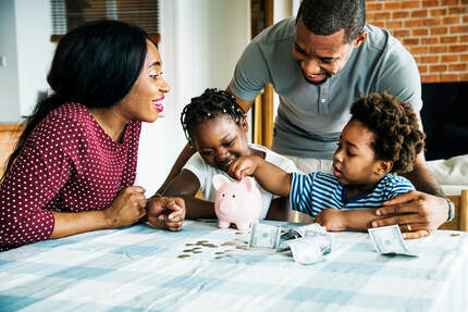 Picture of a mom and dad at a table with their two children while the children count money and place it into their piggy bank
