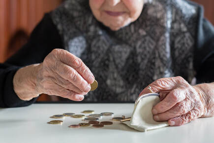 Picture of elderly woman sitting at a table placing coins into her white change purse