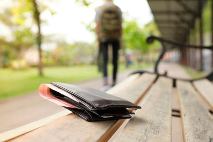 Picture of a wallet left behind on a park bench while someone walks away in the background