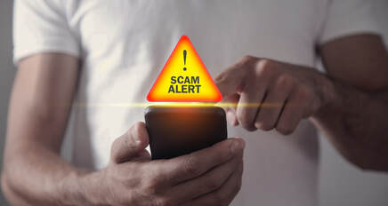 close up picture of a man touching the screen of his cell phone with an illuminated Scam Alert warning sight floating above it