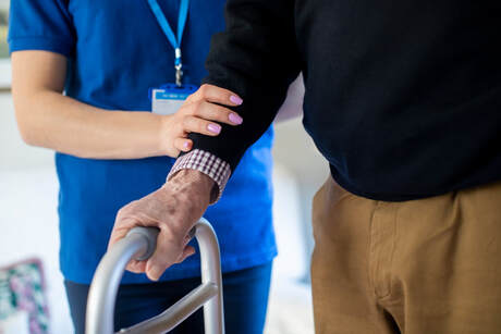 Picture of female nurse assisting elderly male patient using a walker