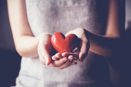 Close-up photo of a woman holding a red heart in front of her in her cupped hands