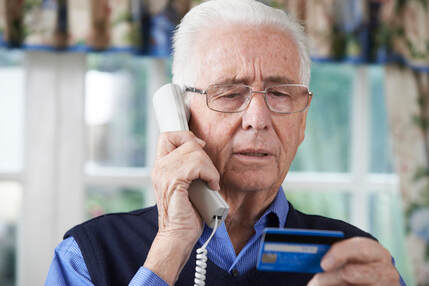 Picture if elderly man talking on the telephone while holding his blue credit card and reading the numbers